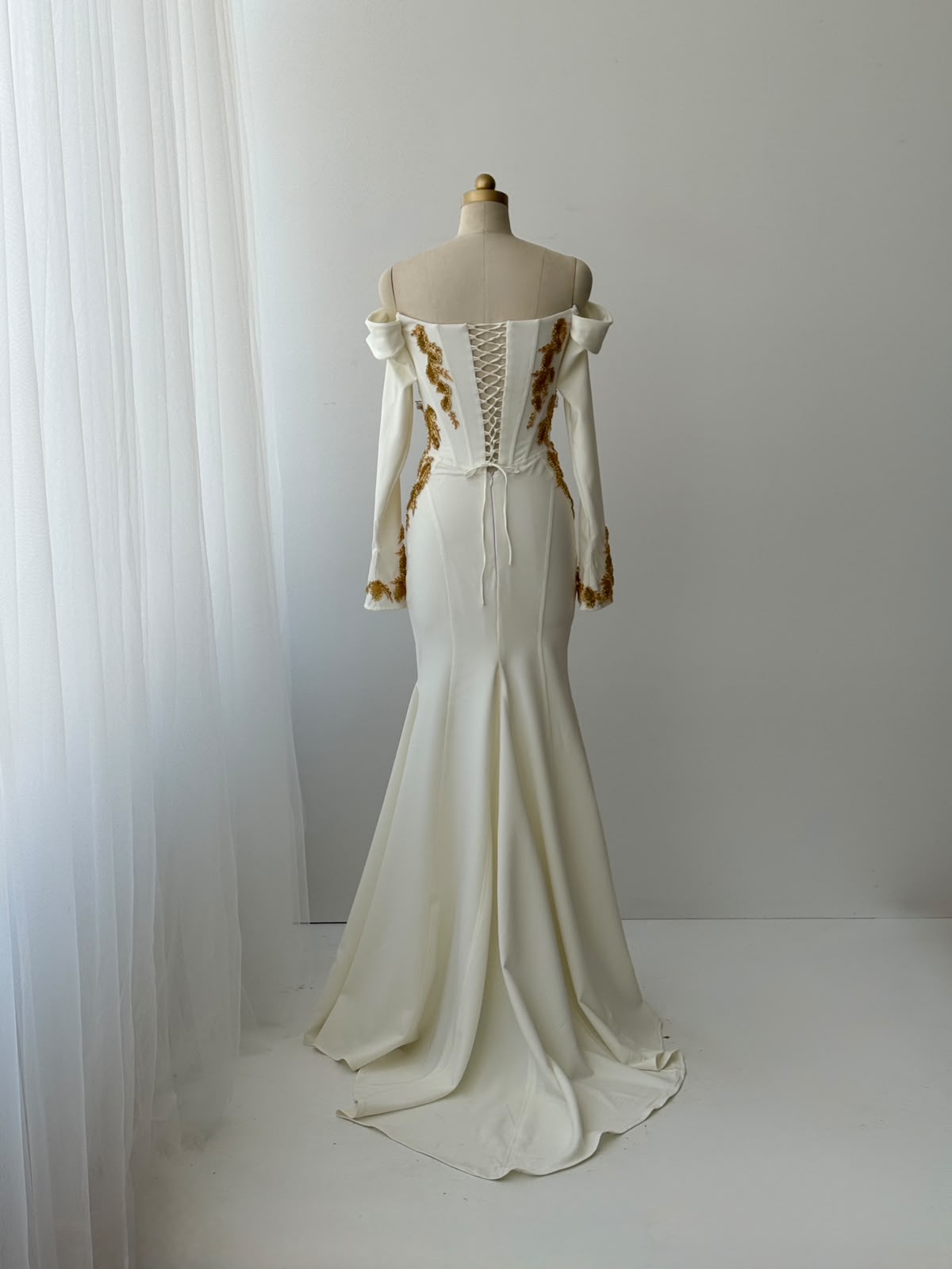 White mermaid bridal gown with long off the shoulder sleeves and gold embroidery