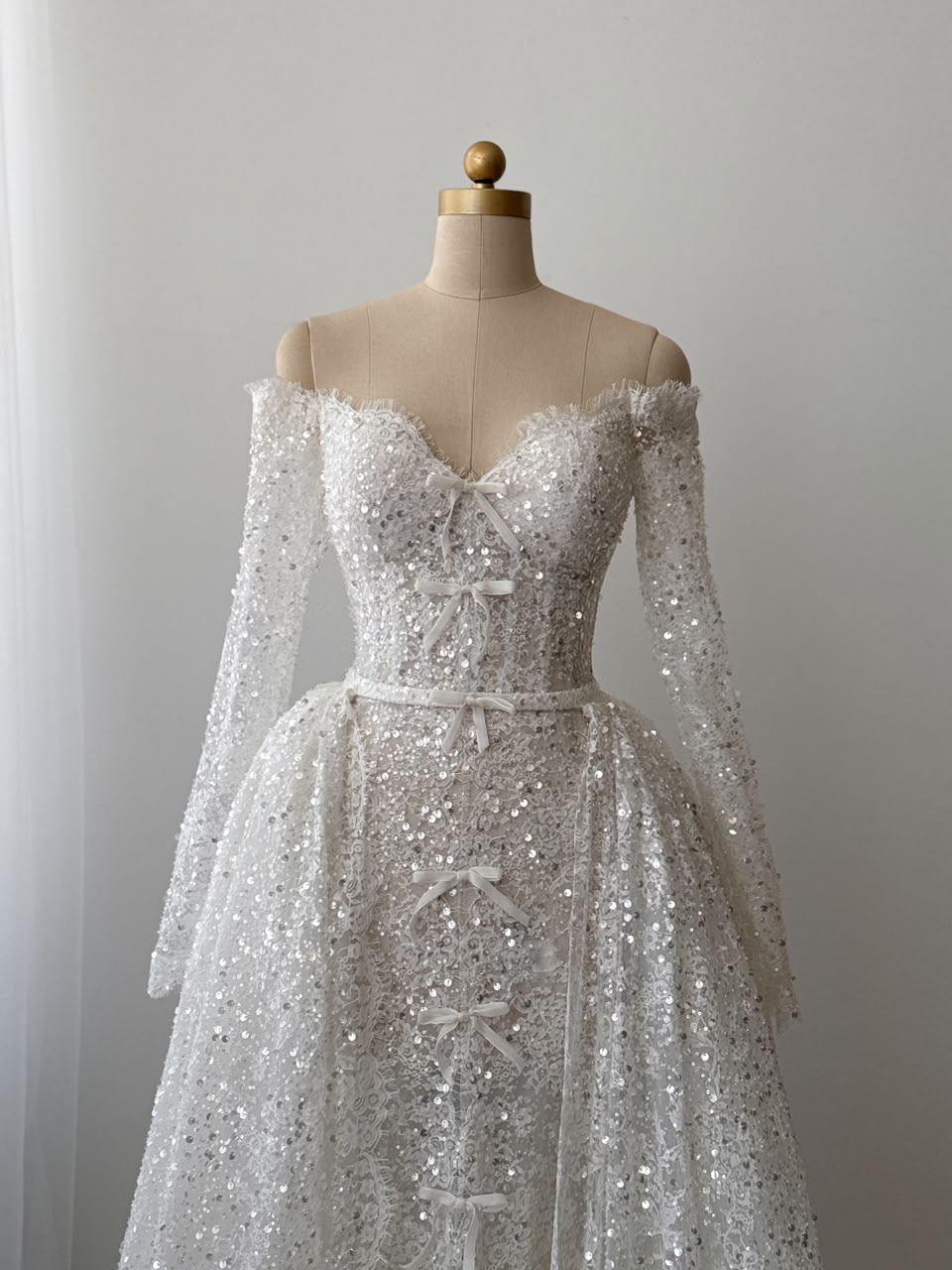 White A-Line bridal gown with long off the shoulder sleeves, sequins, detachable overskirt and embroidered bows