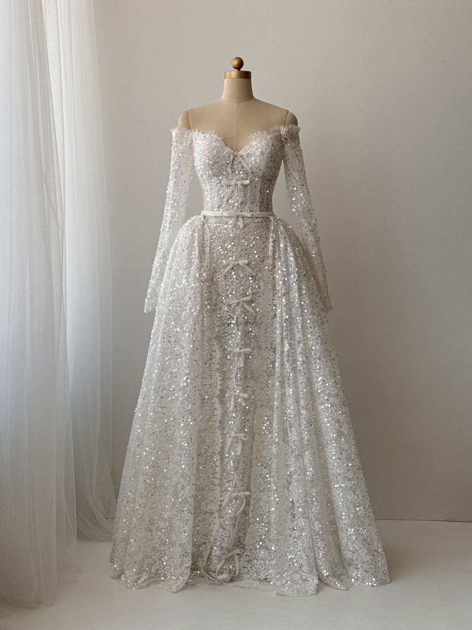 White A-Line bridal gown with long off the shoulder sleeves, sequins, detachable overskirt and embroidered bows