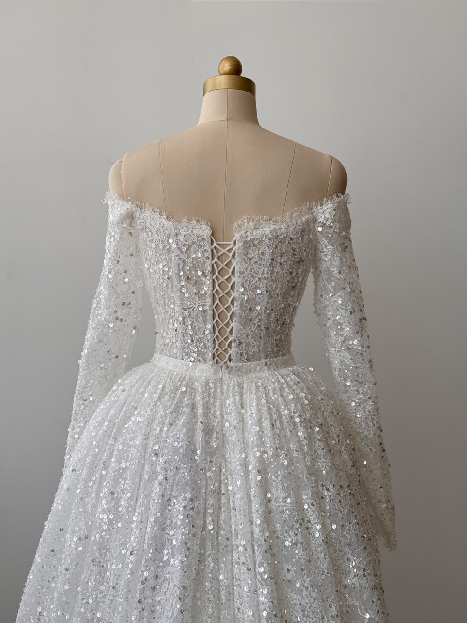 White A-Line bridal gown with long off the shoulder sleeves, sequins, detachable overskirt and embroidered bows